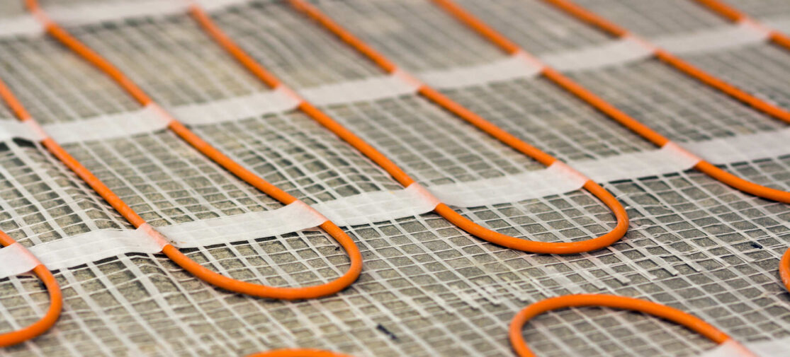 Instalator montuje elektryczne maty grzewcze na podłodze, przygotowując system ogrzewania w nowoczesnym domu.