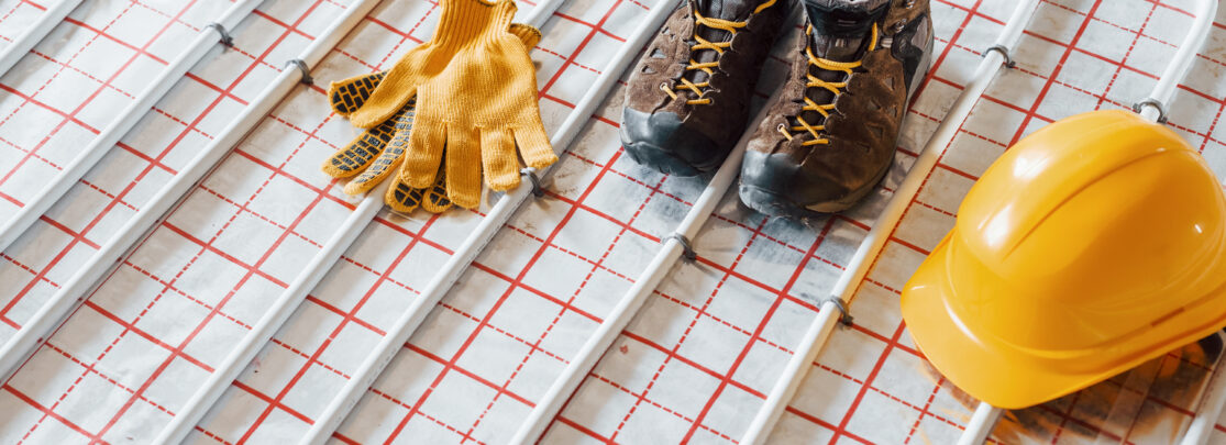 Shoes, hard hat and gloves. Pipes of underfloor heating system. Close up view. No people